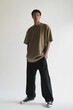 © Sarazabrand - Young Man in Oversized Brown T-Shirt and Black Pants Posing Against White Background