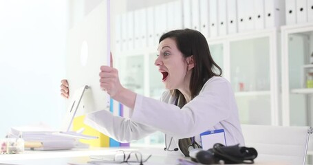 Woman doctor reads news on computer taking monitor to shake at workplace in clinic. Shocked female in uniform expresses astonishment and joy