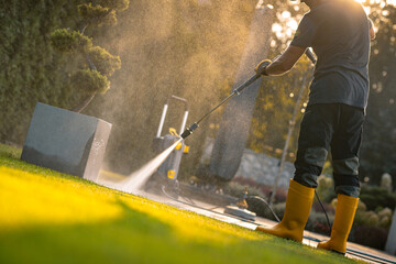 Wall Mural - A Gardener Cleaning a Patio With a Pressure Washer During Golden Hour in a Sunny Outdoor Setting