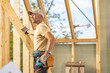 © Tomasz Zajda - Construction Worker Inspecting Wooden Frame Structure in Bright Daylight at a Building Site