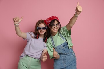 Happy teenage girls showing thumbs up on pink background