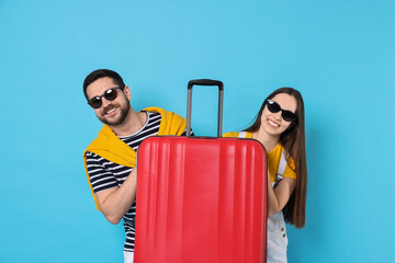 Wall Mural - Happy couple in sunglasses with suitcase on light blue background