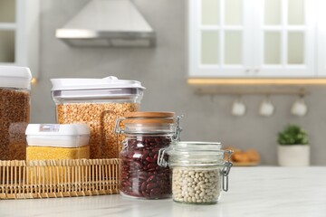 Poster - Different types of cereals and legumes in containers on white marble table in kitchen