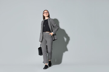 Canvas Print - Beautiful woman in stylish suit and glasses with bag on gray background