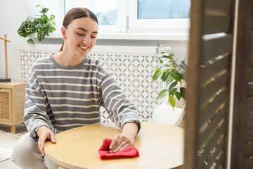 Wall Mural - Beautiful young woman wiping coffee table with rag at home