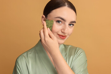 Poster - Beautiful young woman doing facial massage with gua sha tool on beige background