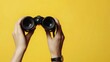 © Khalil - Female hand holds black binoculars on a yellow background. Journey, find and search concept. Banner.