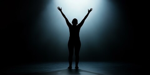 Silhouette of a person with arms raised in the spotlight.