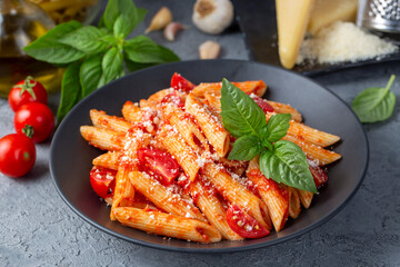 Wall Mural - Classic italian pasta penne alla arrabiata with basil and freshly grated parmesan cheese on dark table. Penne pasta with chili sauce arrabbiata.