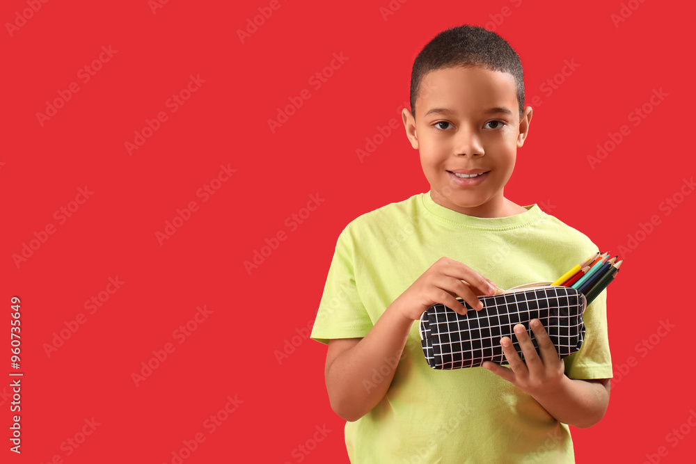 Little African-American boy with pencil case on red background