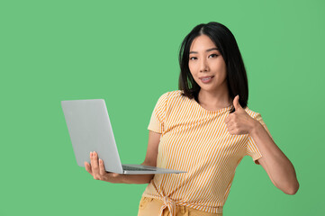 Poster - Young female Asian programmer with laptop showing thumb-up gesture on green background