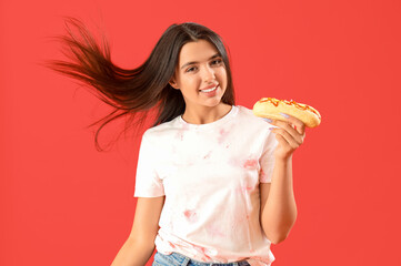 Poster - Pretty young woman with tasty hot dog on red background