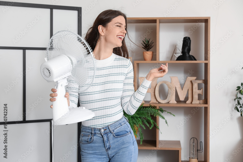 Young woman with blowing electric fan at home