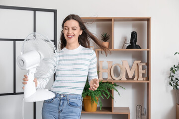 Poster - Young woman with blowing electric fan at home