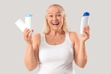 Happy mature woman with bottles of shampoo on light background