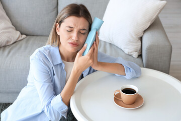 Wall Mural - Young woman with hot-water bottle and cup of coffee suffering from tooth ache at home