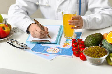 Wall Mural - Young female nutritionist with glass of juice and healthy food writing diet plan in office, closeup