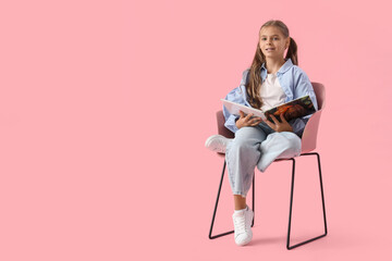 Wall Mural - Cute schoolgirl with book sitting in armchair on pink background