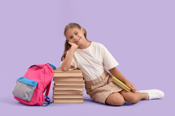 Wall Mural - Cute schoolgirl with books and backpack sitting on lilac background