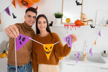 Poster - Young happy couple decorating kitchen with garlands for Halloween party