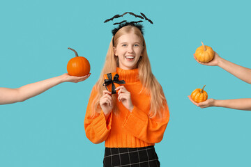 Poster - Beautiful young happy woman in headband with Halloween gift box and hands holding pumpkins on blue background