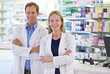 © ArcursForPI/peopleimages.com - Pharmacy, man and woman in portrait with confidence, smile and prescription drugs in clinic. Teamwork, advice and pharmacist with arms crossed, medicine and pills for medical service at counter