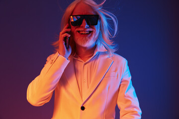 Wall Mural - Stylish older man with long white hair and sunglasses engaging in a phone conversation, set against a vibrant colorful background