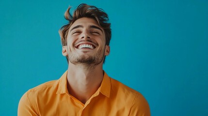 Portrait of a happy handsome man in a orange shirt, laughing against a blue background with copy space