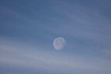 closeup full moon veiled by thin clouds in a dark blue sky