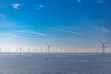 Abstract ethereal view of beautiful giant wind turbines at sea with patchy fog blue sky