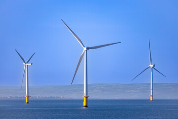 Abstract ethereal view of beautiful giant wind turbines at sea with patchy fog blue sky