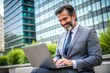 © Introvertia - Happy businessman using laptop outdoors in urban setting