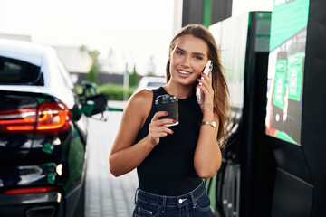 Wall Mural - Having a conversation by phone. A young woman at a gas station with her car