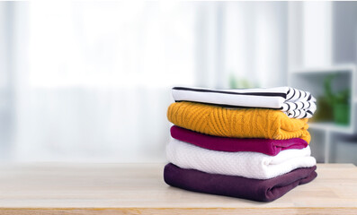 Poster - Stack of knitted jersey clothes on wooden table empty copy space. Folded knitwear, autumn colorful apparel.