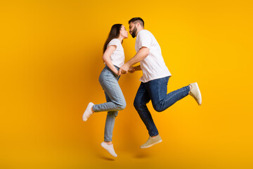 Poster - Full size photo of pretty young male female jump hold hands kissing wear trendy white outfit isolated on yellow color background