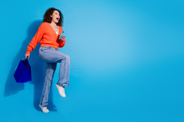 Wall Mural - Photo of wavy haired model woman using smartphone overjoyed running to buy more surprises isolated on blue color background