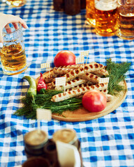 Wall Mural - Platter of grilled sausages served with tomatoes, peppers, and dill on blue and white checkered tablecloth. Concept of Oktoberfest, festival, party, brewery, traditions