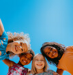 © Abelorz - A photo of diverse, happy children looking down at the camera, smiling and posing for an advertising campaign in front of a blue sky. Group portrait of happy kids huddling. Friendship concept.