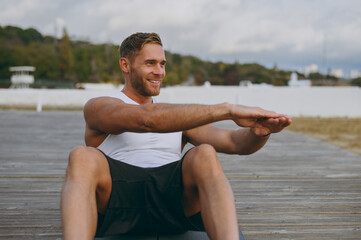 Wall Mural - Young strong sporty fit sportsman man wears sports clothes do abdominal abs exercises at floor, pump press warm up training at sunrise sun over sea beach outdoor on pier seaside in summer day morning.