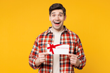 Wall Mural - Young surprised shocked happy man he wears red checkered shirt casual clothes hold gift certificate coupon voucher card for store isolated on plain yellow orange background studio. Lifestyle concept.