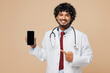 © ViDi Studio - Young Indian doctor man wear white medical gown suit work in hospital clinic office hold use show blank screen mobile cell phone isolated on plain beige background studio. Healthcare medicine concept.