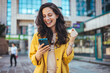 © Dragana Gordic - Happy Woman Celebrating Success While Using Smartphone Outdoors
