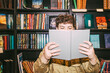 © Maskot - Young man reading book near shelf in bookstore