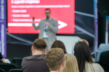 Wall Mural - Business professional giving a presentation during a conference. Audience members attentively listening to the speaker.