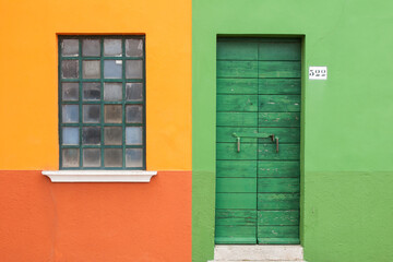 A window and a door on green, red and yellow wall in the island of Burano, Venice, Italy.