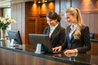 © Introvertia - Two smiling receptionists at hotel front desk computer terminals in modern lobby