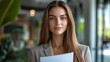 © Nottenaj - 5. Half-body image of a confident office worker woman with long hair, wearing a blazer and presenting a document, in a bright and modern office setting