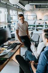 Young male programmer discussing with colleagues sitting on chair at office