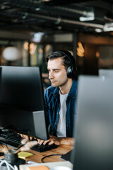 Young computer programmer typing on desktop PC with wireless headphones in office