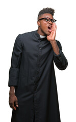 Young african american priest man over isolated background shouting and screaming loud to side with hand on mouth. Communication concept.